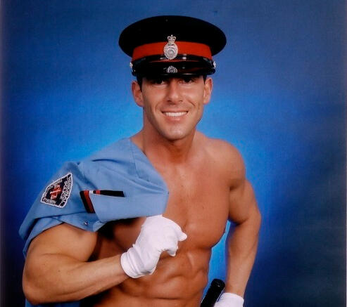 Professional photo of performer Miguel Storm smiling in his police costume with shirt draped over his shoulder